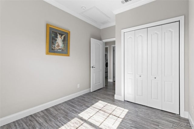 unfurnished bedroom with attic access, baseboards, wood finished floors, crown molding, and a closet