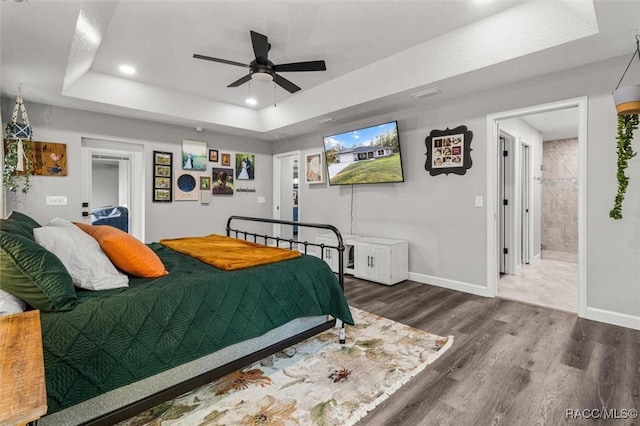 bedroom with dark hardwood / wood-style flooring, ensuite bathroom, a raised ceiling, and ceiling fan