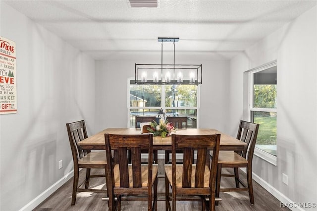 dining area featuring a healthy amount of sunlight, dark hardwood / wood-style flooring, a textured ceiling, and an inviting chandelier