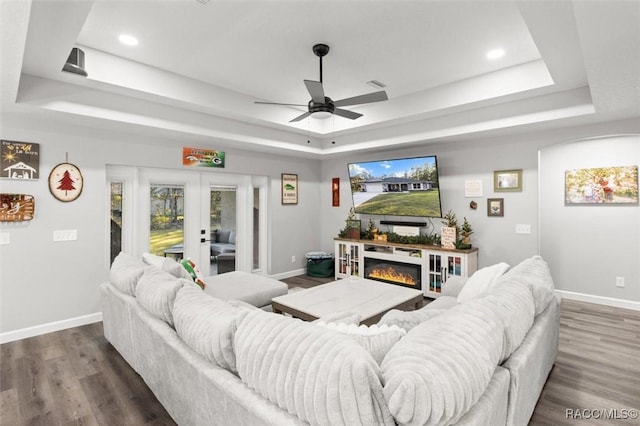 living room featuring a tray ceiling, ceiling fan, dark hardwood / wood-style flooring, and french doors