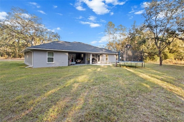 rear view of house with a lawn, a trampoline, and a patio