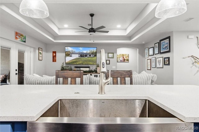 kitchen with pendant lighting, ceiling fan, a raised ceiling, and sink