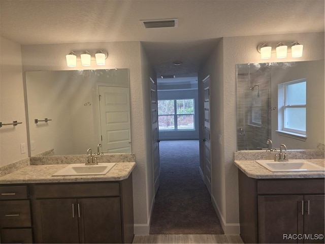 bathroom with a textured wall, visible vents, a sink, and tiled shower