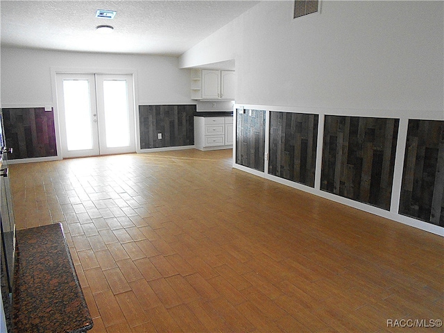 unfurnished living room with french doors, a textured ceiling, light hardwood / wood-style flooring, and wood walls