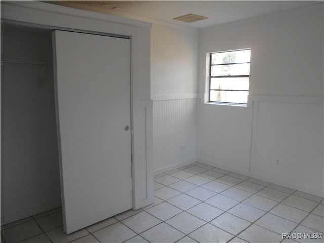 unfurnished bedroom with light tile patterned floors, crown molding, and a closet