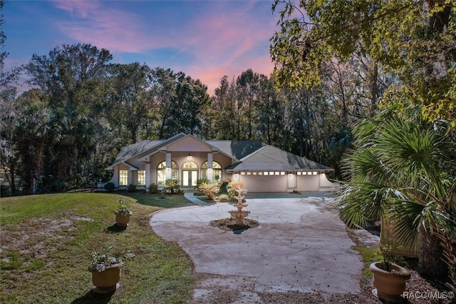 view of front of home featuring french doors, a yard, stucco siding, a garage, and driveway