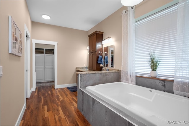 full bath with wood finished floors, vanity, baseboards, and a bath