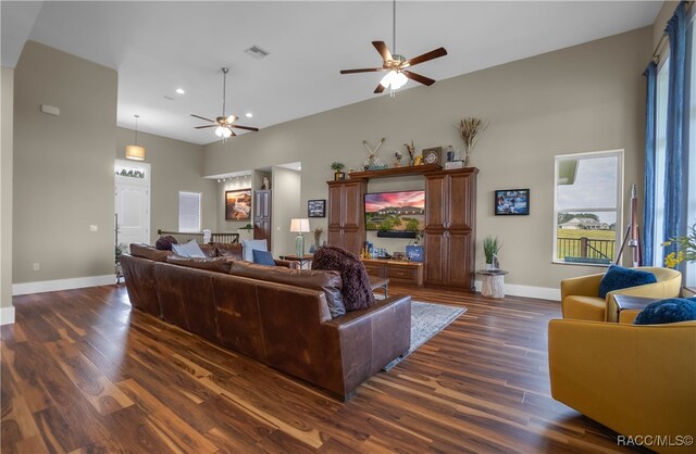 living area with dark wood-type flooring, a high ceiling, baseboards, and a ceiling fan