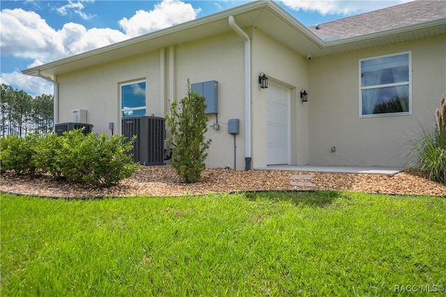 exterior space with stucco siding, a shingled roof, a lawn, central AC unit, and a garage