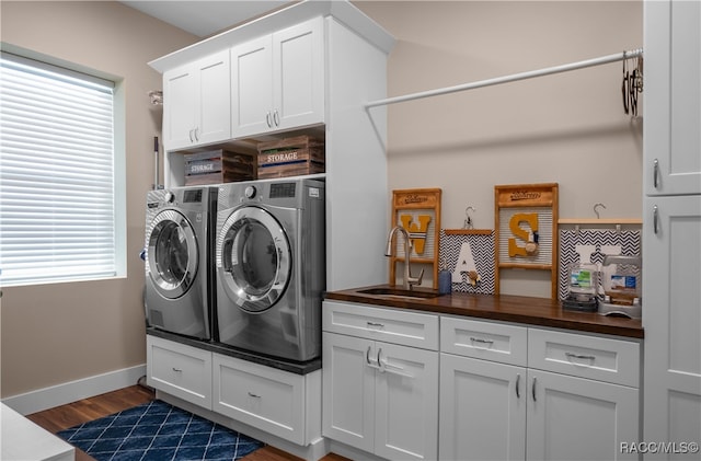 laundry room featuring washing machine and dryer, a sink, baseboards, cabinet space, and dark wood finished floors