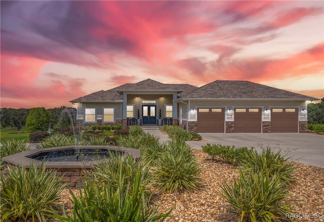 prairie-style house featuring driveway, french doors, an attached garage, and stone siding