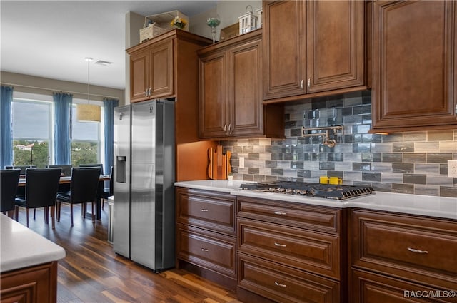 kitchen with stainless steel appliances, light countertops, decorative backsplash, brown cabinets, and dark wood-style floors