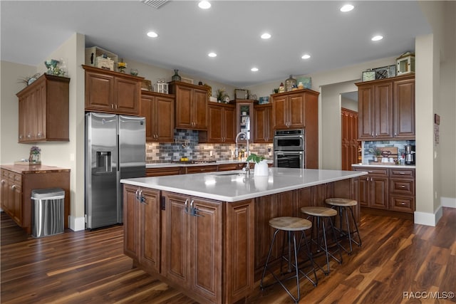 kitchen featuring an island with sink, a sink, appliances with stainless steel finishes, and dark wood-type flooring