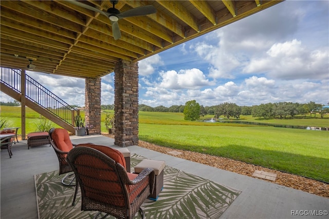 view of patio with ceiling fan, stairway, and a water view