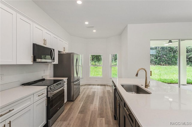 kitchen with light hardwood / wood-style flooring, sink, light stone counters, stainless steel appliances, and white cabinets