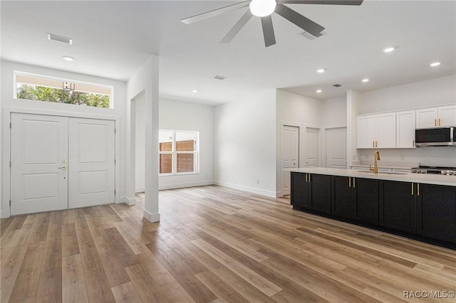 kitchen featuring a center island with sink, light hardwood / wood-style flooring, ceiling fan, sink, and white cabinetry