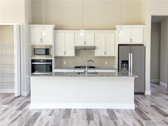 kitchen featuring light stone counters, decorative backsplash, a center island with sink, white cabinets, and appliances with stainless steel finishes