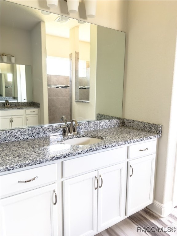 bathroom featuring hardwood / wood-style flooring, vanity, and tiled shower