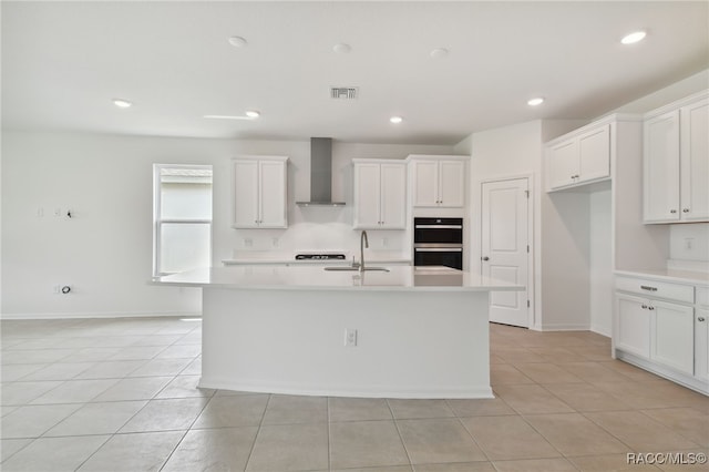 kitchen with white cabinetry, wall chimney range hood, and an island with sink