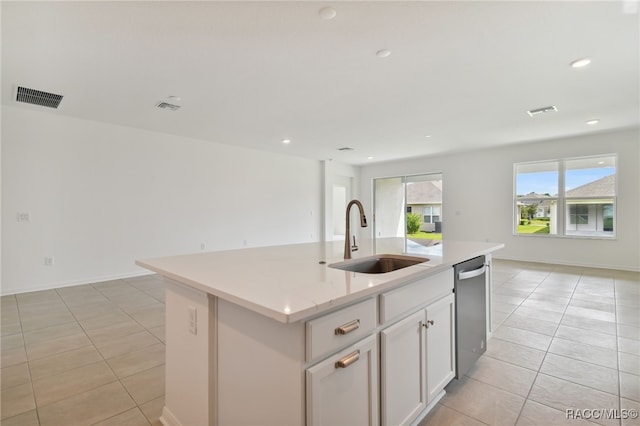 kitchen with stainless steel dishwasher, sink, a center island with sink, white cabinets, and light tile patterned flooring