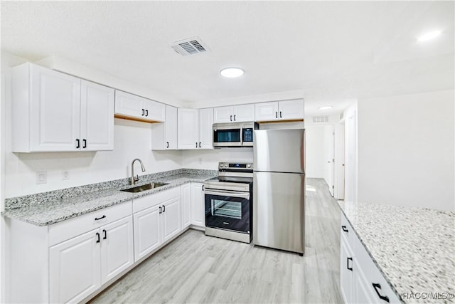 kitchen with sink, stainless steel appliances, white cabinetry, and light wood-type flooring