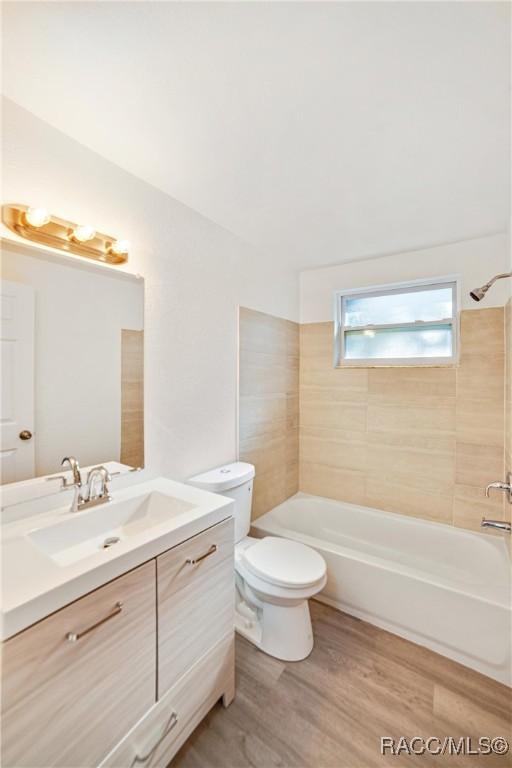 full bathroom featuring vanity, hardwood / wood-style floors, tiled shower / bath combo, and toilet