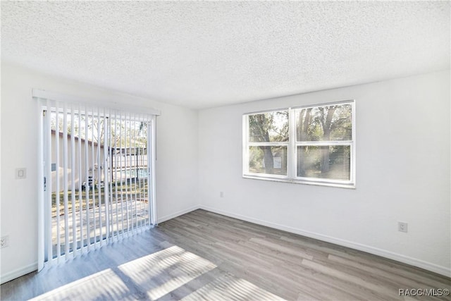 empty room with a textured ceiling, hardwood / wood-style floors, and a healthy amount of sunlight