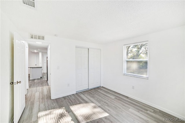 unfurnished bedroom featuring light wood-type flooring, a closet, and a textured ceiling