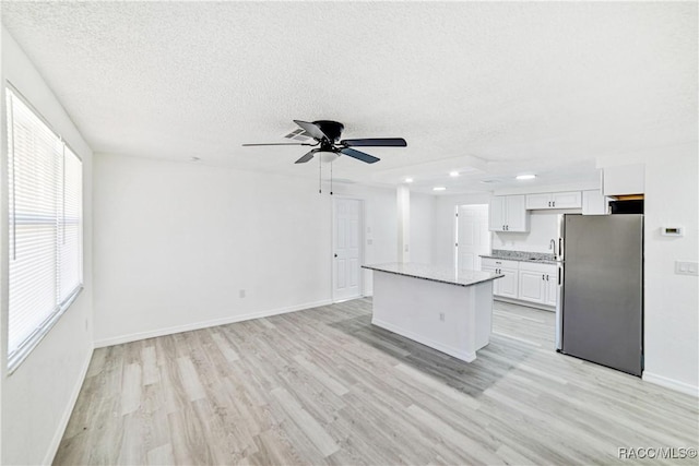 kitchen with white cabinetry, a textured ceiling, a center island, light wood-type flooring, and stainless steel fridge