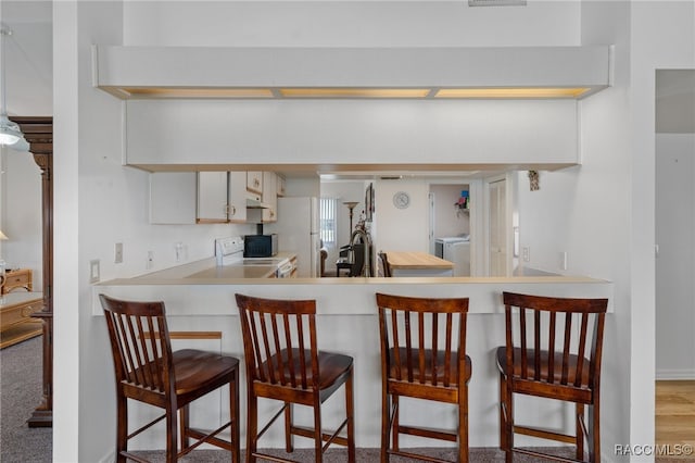 kitchen featuring stove, white cabinets, a kitchen breakfast bar, light hardwood / wood-style floors, and kitchen peninsula