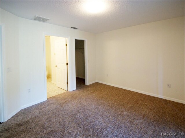 unfurnished bedroom with light carpet, a closet, a spacious closet, and a textured ceiling