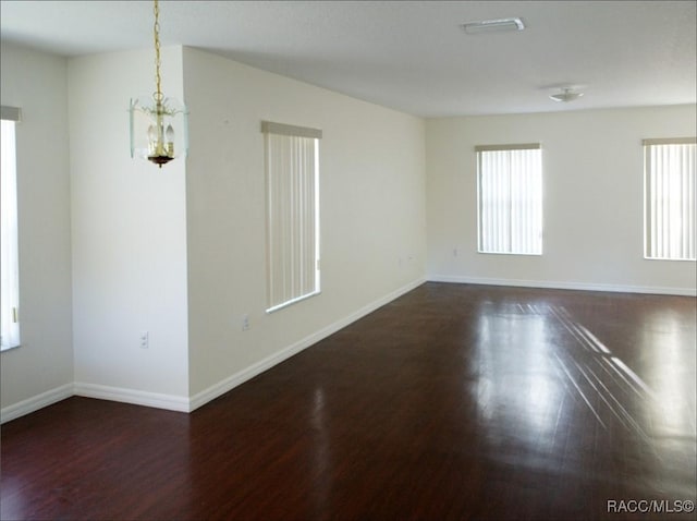 empty room with dark hardwood / wood-style flooring and a chandelier