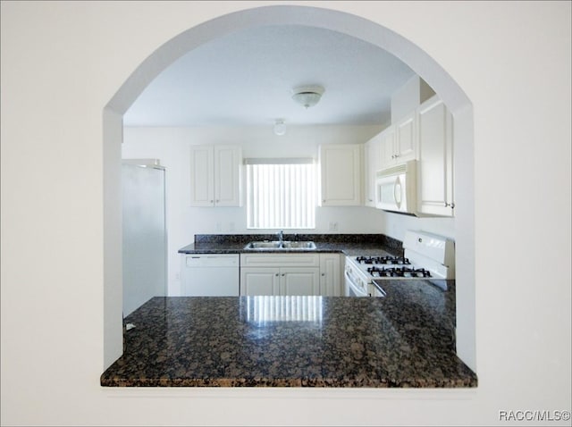 kitchen featuring white appliances, white cabinetry, dark stone counters, and sink