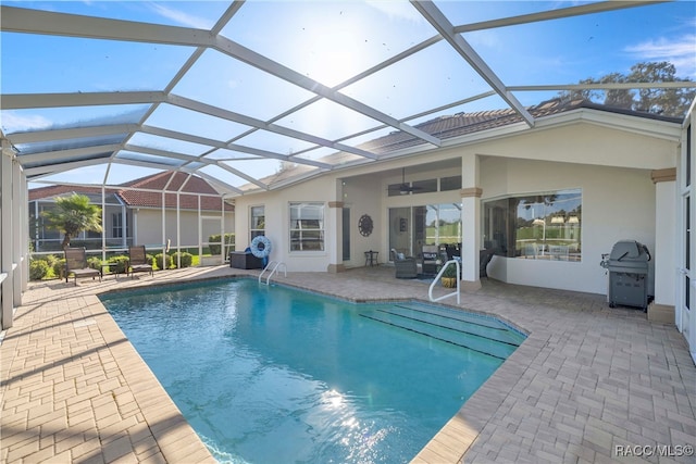 view of pool with area for grilling, a patio, glass enclosure, and ceiling fan