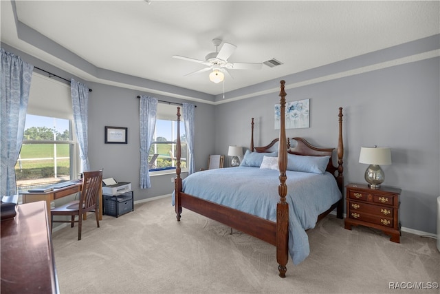 carpeted bedroom with ceiling fan, a raised ceiling, and multiple windows