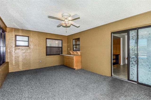 unfurnished room featuring ceiling fan, dark carpet, and a textured ceiling