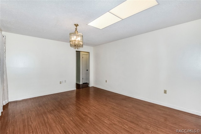 empty room featuring a textured ceiling, dark wood-type flooring, and a skylight