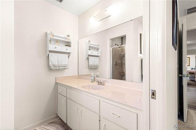 bathroom featuring a shower with door, vanity, and a textured ceiling