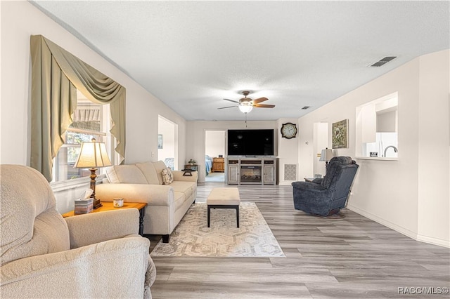 living room with ceiling fan, wood-type flooring, and a textured ceiling