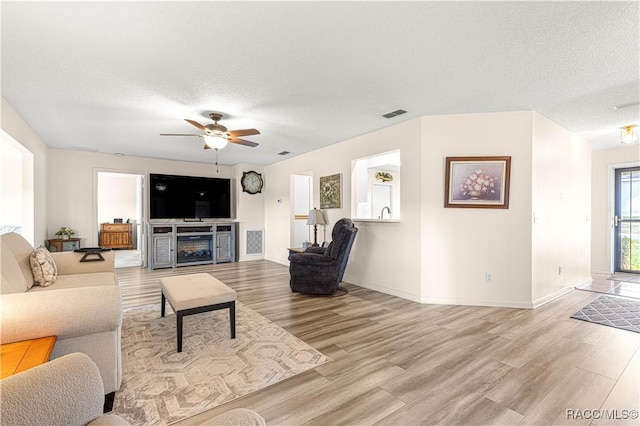 living room with a textured ceiling, ceiling fan, a fireplace, and light hardwood / wood-style flooring