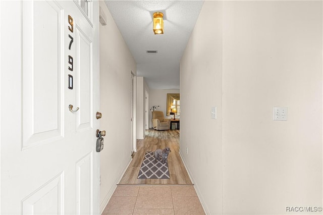 corridor with light tile patterned flooring and a textured ceiling