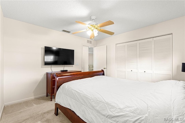 bedroom with ceiling fan, a closet, light colored carpet, and a textured ceiling