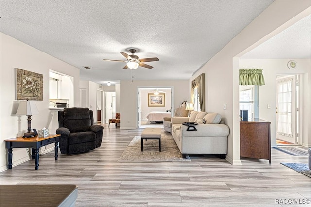 living room featuring ceiling fan, light hardwood / wood-style flooring, and a textured ceiling