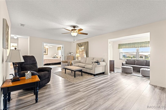 living room featuring ceiling fan, a textured ceiling, and light wood-type flooring