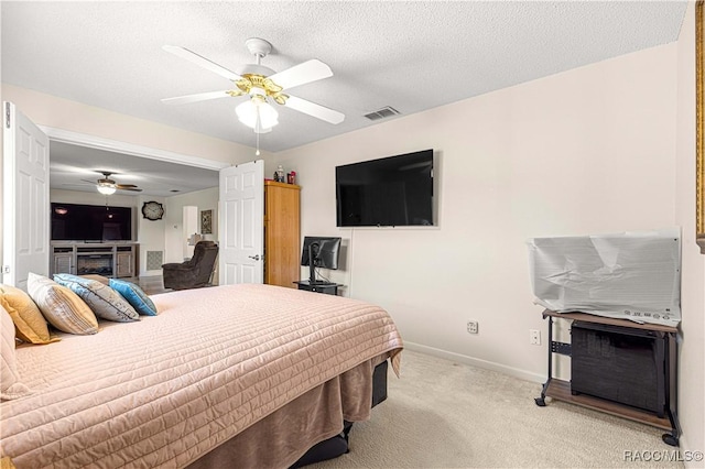 bedroom with ceiling fan, a fireplace, light carpet, and a textured ceiling