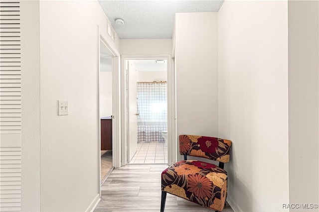 hallway with a textured ceiling and light hardwood / wood-style flooring