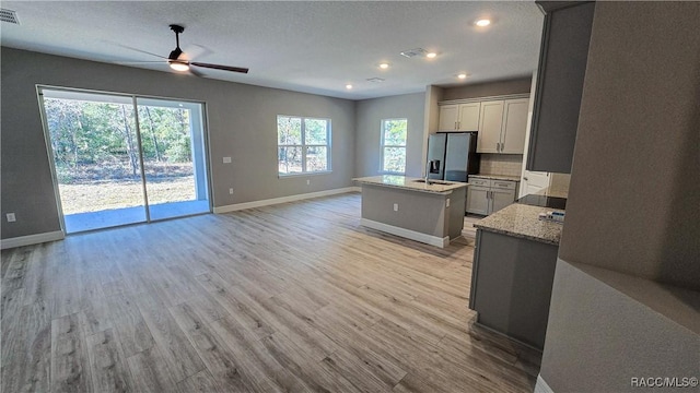 kitchen with gray cabinets, an island with sink, refrigerator with ice dispenser, light hardwood / wood-style floors, and light stone countertops