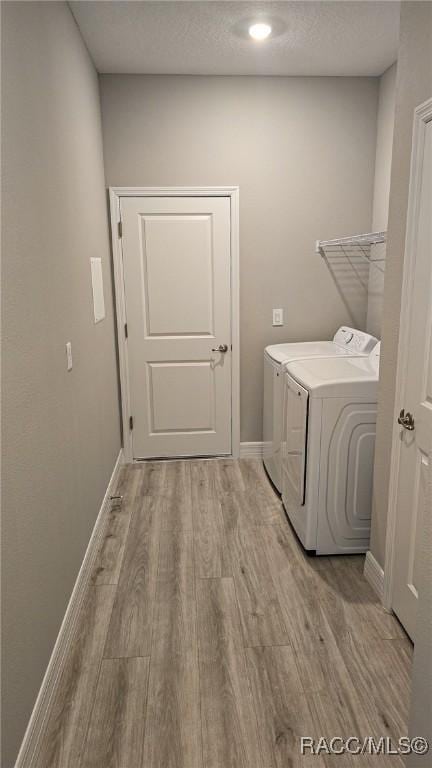 laundry room with a textured ceiling, light hardwood / wood-style floors, and washing machine and clothes dryer