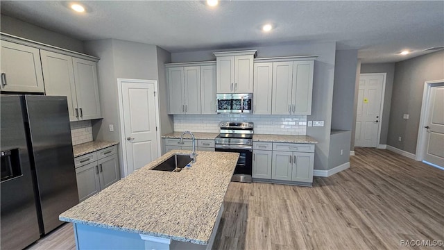 kitchen featuring sink, light stone counters, stainless steel appliances, a center island with sink, and light wood-type flooring