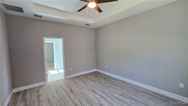 empty room with a tray ceiling, ceiling fan, and light wood-type flooring